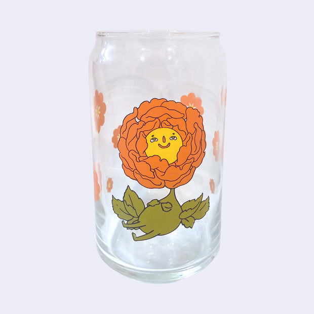 Glass cup with a flat base and slightly inward lip. Features a graphic of a cartoon style orange peony, sitting with a smiling face and a chubby green body made out of stems and leaves. Around the rest of the glass are orange flowers.