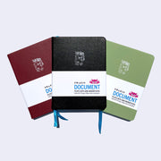 Set of 3 pleather covered notebooks, all featuring a small robot carrying a flag that reads "Giant Robot" in the upper center of each journal. Colors are: burgundy, black and sage green.