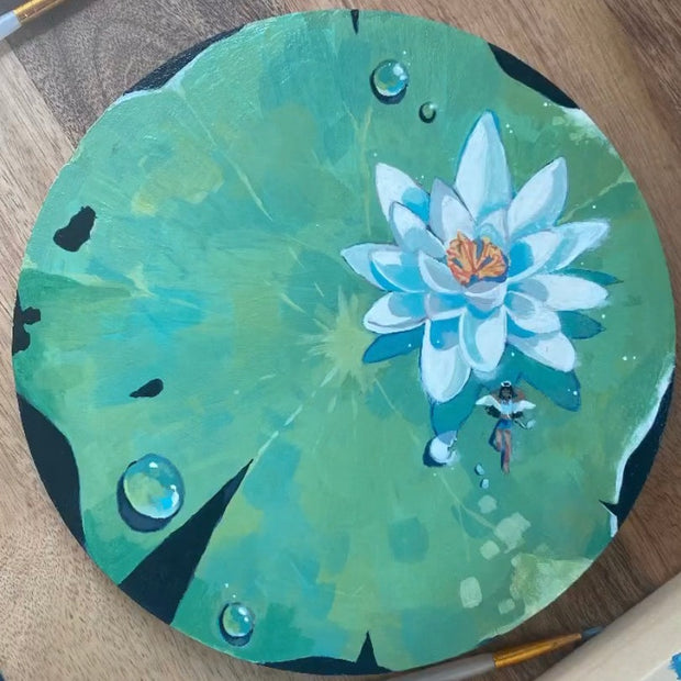 Painting on round wood panel of a large lily pad with a white flower. A small girl with angel wings sits below the flower.