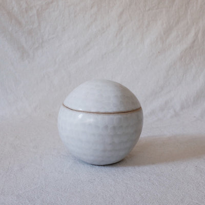 Small ceramic sculpture of a sphere with a lid, white with very faint gray dots.