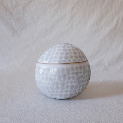 Small ceramic sculpture of a sphere with a lid, white with very faint gray dots.