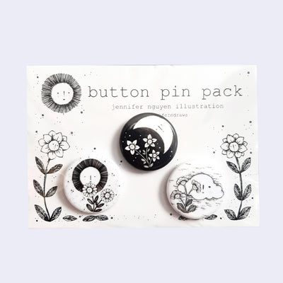 3 black and white tin buttons on a white backing card with floral illustrations. Pins include: sun with flowers, moon with flowers and clouds with flowers.