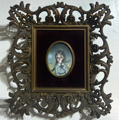 Illustration in a small oval within a black velvet mat and ornate bronze frame. Illustration is of a small girl with braids and a fancy blue dress, with tears streaming down her face as she looks off to the side.