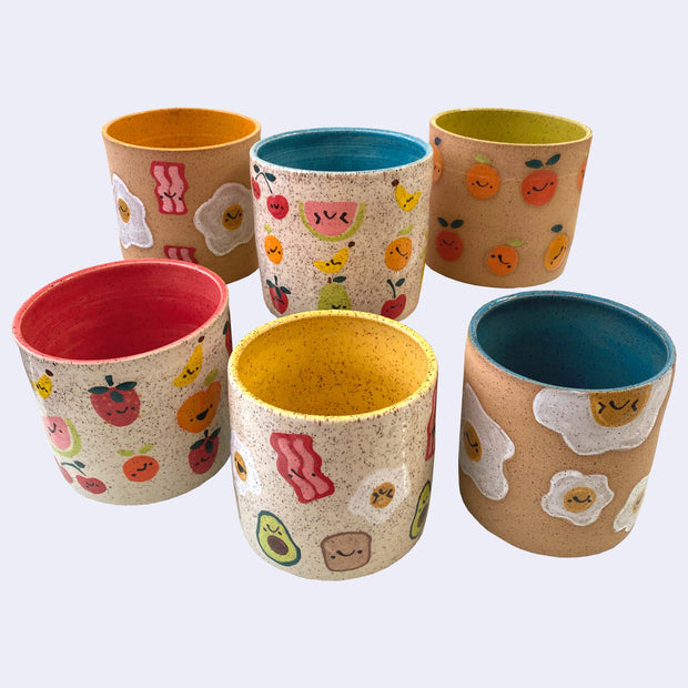 6 ceramic planter pots, with bright insides of all colors including blue, orange, green and red. Exteriors have little drawings of foods, such as fruits or breakfast items.