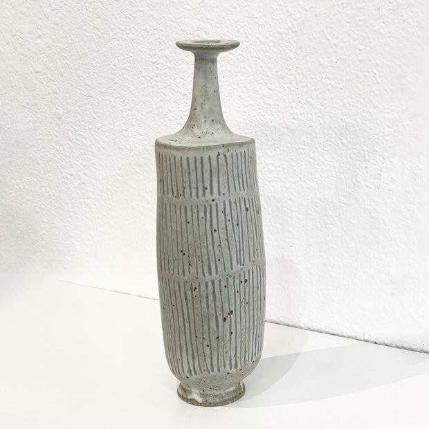 Vase with skinny fluted top with many lines and black dots.