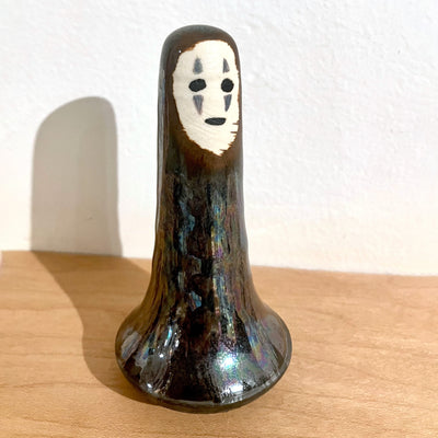 Ceramic sculpture of a tall skinny No Face from Spirited Away, with a large base that is rounded on the bottom to allow the piece to wobble.