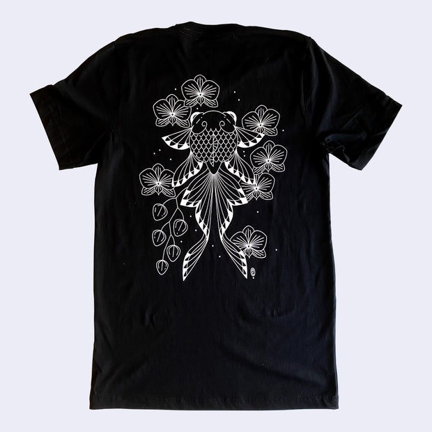 Back of a black t-shirt with white line art illustration of a goldfish a long tail and slightly bulged eyes. Around it are orchids, mostly bloomed but a few still buds.