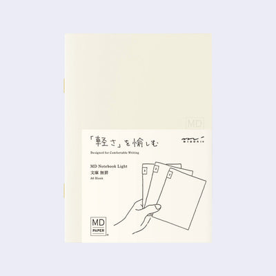 Cream colored blank cover journal within packaging with a cream insert that has Japanese writing and an illustration of a hand holding 3 notebooks.