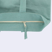 Close up of a zip top teal tote bag, featuring the cream colored lined zipper.