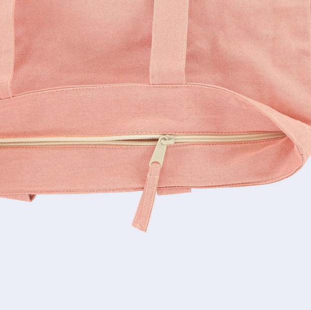 Close up of the top of a pink tote bag, displaying a cream colored zip closure.