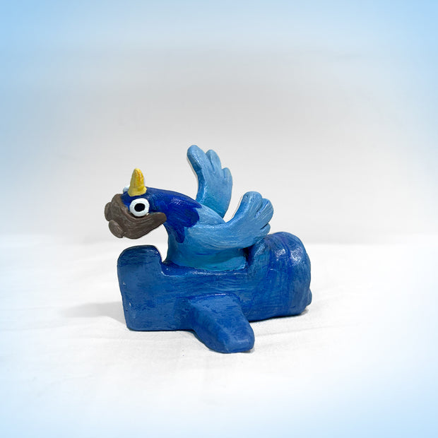 Small sculpture of a cartoon style blue pigeon, its head cocked back and wearing a leather flying cap. It sits in a simplistic blue plane. 