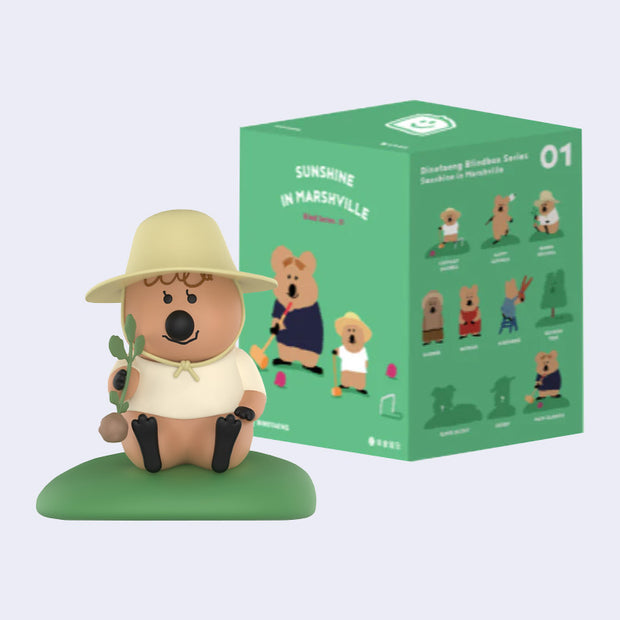 Small figure of a cartoon quokka, wearing a farmer's hat and holding an uprooted vegetable. They sit in front of their product packaging.