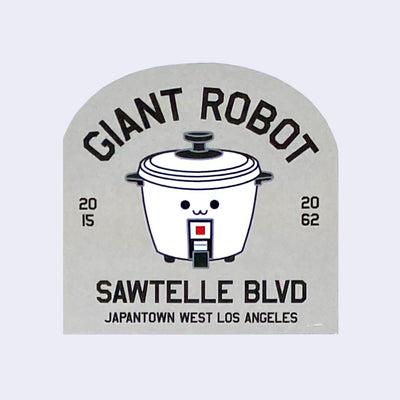 Grey die cut arc shaped sticker of an illustrated smiling rice cooker. Above it reads "Giant Robot" and below reads "Sawtelle Blvd Japantown West Los Angeles"
