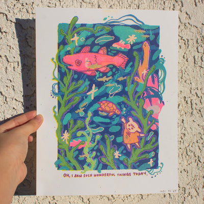 Risograph print of a stylistically messy underwater scene, with kelp, a large pink fish and a small pink and orange turtle. A small dog character reaches out to the turtle.