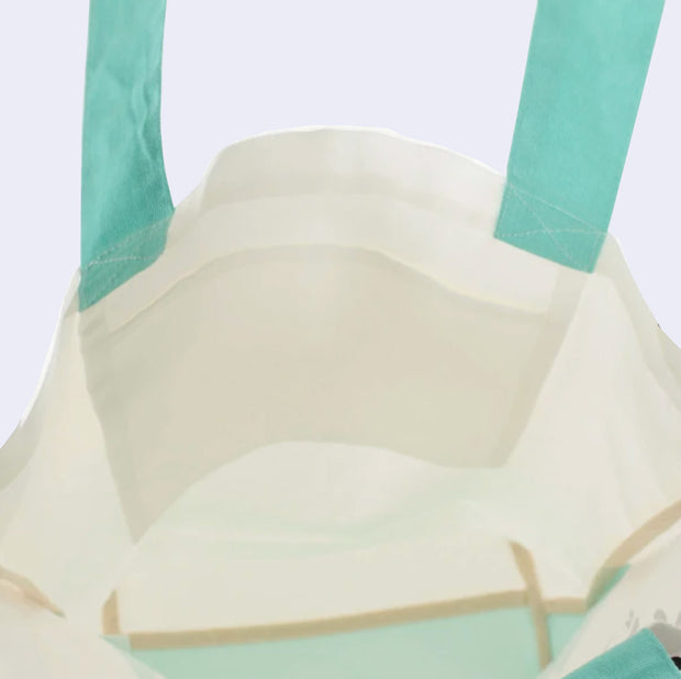 Inside view of cream colored tote bag with teal straps, showing a small inner pocket.