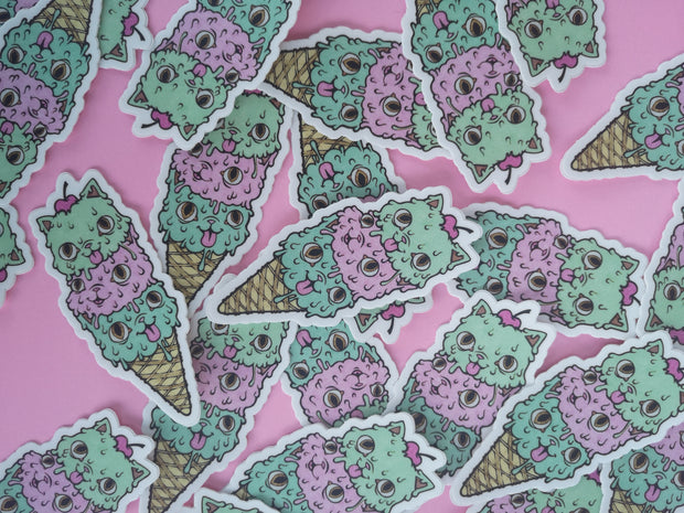 Die cut sticker of 3 cat shaped ice cream scoops, dripping with wide eyed happy expressions. There is a cherry on top and they're stacked in a sugar cone.