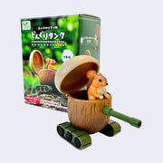 Small plastic squirrel inside of a tank made out of an acorn. It stands in front of its product packaging.