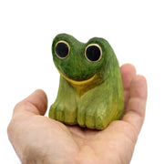 Small whittled wooden sculpture of a green frog with very large eyes, mostly large black circles with a thin yellow outline.