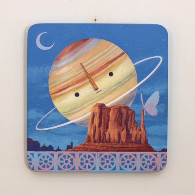 Painting of Saturn, with a simple cartoon face. It hangs largely behind a rocky bluff with a large butterfly resting atop them. A small row of breeze blocks lines the bottom of the piece.