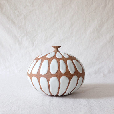 Small terracotta colored clay vase with large semi raised white ovals all around it, as a pattern.