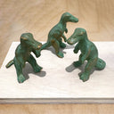 Three green dinosaur figurines on a light wooden surface