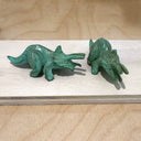 Two green dinosaur figurines on a wooden surface