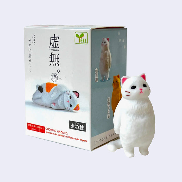 Figure of a fluffy, chubby white cat standing on its hind legs and staring off into the distance, as if zoning out. It stands next to its product packaging.
