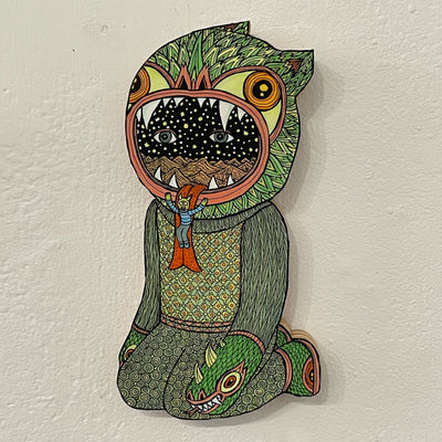 Illustrated wood cut of a figure sitting on its knees, wearing a monster head as a hat, with a tongue coming out and a small goblin sliding down it. Within the monster mask is a starry night sky with sand dunes and two eyes looking out.