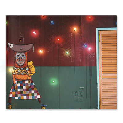 Os Gemeos cover, an illustrated character in wildly patterned outfit stands in front of a two tone wall with Christmas lights.