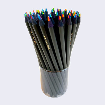 Clear cup holding many black sharpened pencils with rainbow color tips. 