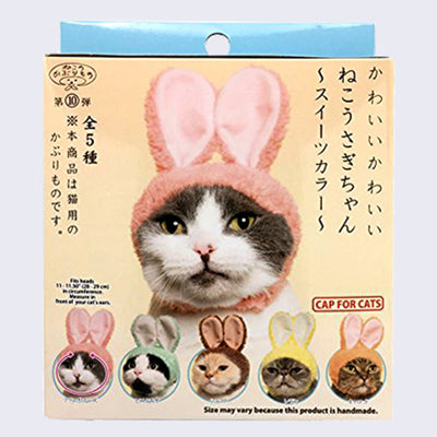 A yellow and blue blind box packaging with a gray and white cat wearing a snug fitting cap with pink, fluffy rabbit ears. 5 total bunny cap designs show at the bottom, including pink, green, brown, yellow and orange. Japanese script is written on the box. 