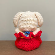 Crochet plush sculpture of a cute looking white rabbit with simple features and a smile, sitting within a red pouch that is tied up with a gold string and has Chinese script on a gold patch on the center of the pouch.