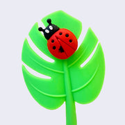 Close up of pen topper, a green monstera-style leaf with a lady bug on it.
