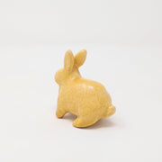 Yellow ceramic bunny with no facial features, looking slightly alert.