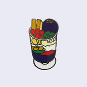 Enamel pin of illustrated Filipino dessert, halo halo,  in a cup with purple, red, yellow and green fruit within the cup.