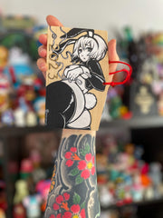 A rectangular wooden token on red string, with illustration of an anime style woman with a curvaceous body and bunny costume lingerie, looking back and exposing her butt that has a cotton bunny tail on it. She wears bunny ears and 2023 is written along the bottom. Painting is black and white.