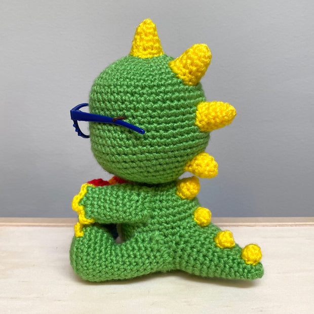 Back view of a crocheted sculpture of a chibi Kaiju, green with yellow spikes and nails.