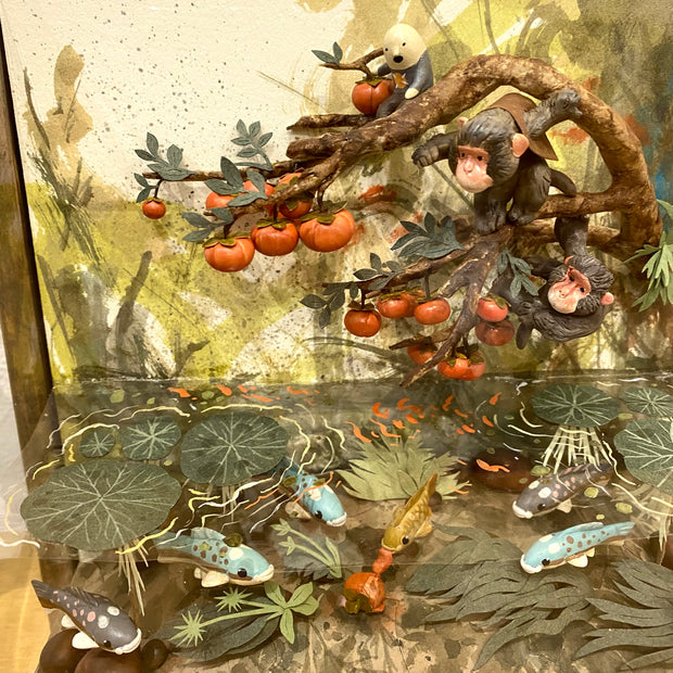 Diorama like sculptural piece encased in a glass box with a wooden mount framing. Elaborate scene of two monkeys hanging onto the branch of a persimmon tree, looking at the water below them, filled with water plants and various colored fish.