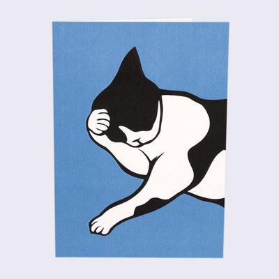 The front of note card is shown. The notecard has an illustration of a tuxedo cat laying on its side and cleaning his face its paw.