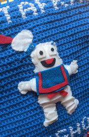Close up of a sewn cartoon Stay Puft Marshmallow Man, with its mouth open and arms extended.