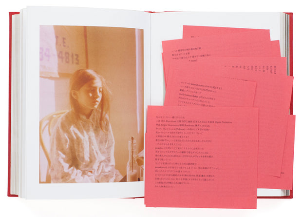 Open two page book spread. Left page is a sepia colored photograph of a young girl. Right page is many red notecards with small Japanese typed words one one another.