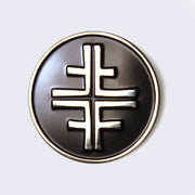 Circular enamel pin, black with silver lining. In the center is a silver shape, the band Jawbreaker's logo. Logo is an elongated plus sign with four additional lines coming out the sides, with an intersection running through the middle and sides of the main shape.