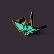 Enamel pin of an origami crane glowing in the dark.