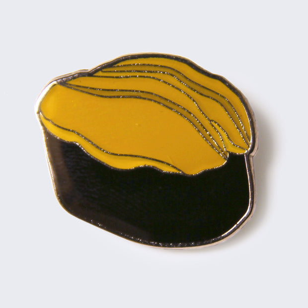Enamel pin of a piece of yellow sea urchin sushi. The piece of sea urchin is atop a black seaweed wrap.