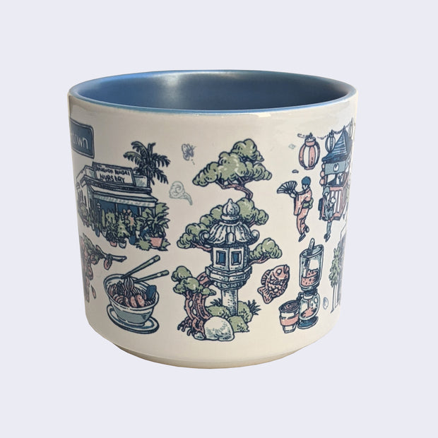 White ceramic mug with a metallic blue interior and various illustrations on it, all within a color scheme of blue, pink, white and green. Illustrations include an exterior of a plant nursery, a bowl of ramen, a stone lantern with a tree behind it, and a taiyaki.