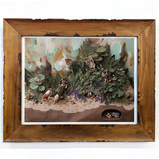 Photograph of a detailed clay and paper diorama. A person walks with an owl through a lush forest setting, waving to the various raccoons standing within the scene. 2 raccoons can be seen buried under the ground.