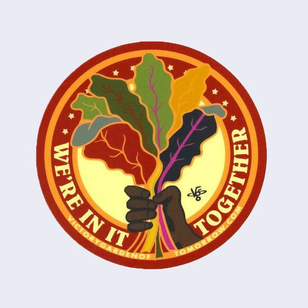 Red and orange bordered sticker with an illustration of a tan hand holding a bunch of colorful leafy greens. "We're in it together" is written in bold all caps yellow font.