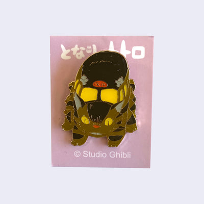 Enamel pin of Catbus with a slight smile, facing head on and looking down. On a light pink backing card with Japanese writing.