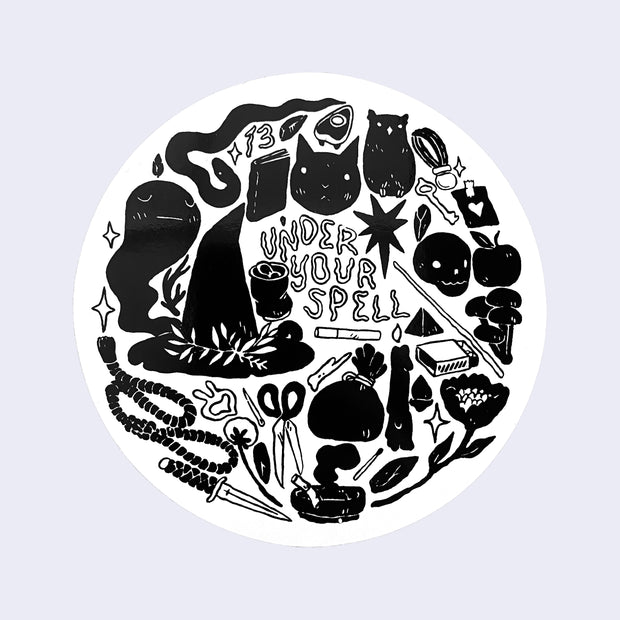 White circle sticker with drawings of objects used to cast magic spells. Stylized text in the center says under your spell.
