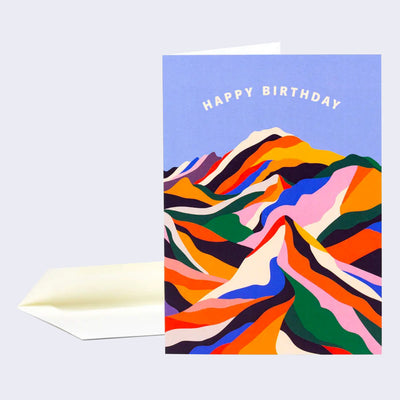 Greeting card with a purplish blue background and many colorful mountain ranges, made out of simplistic shapes. "Happy Birthday" is written across the top in cream colored font.